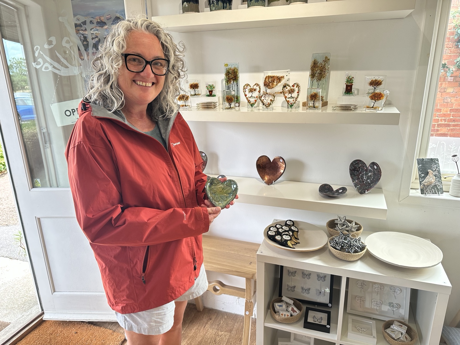 Emma Fairbrother holding a handmade ceramic heart beside her Raku ceramics at Wistow Gallery