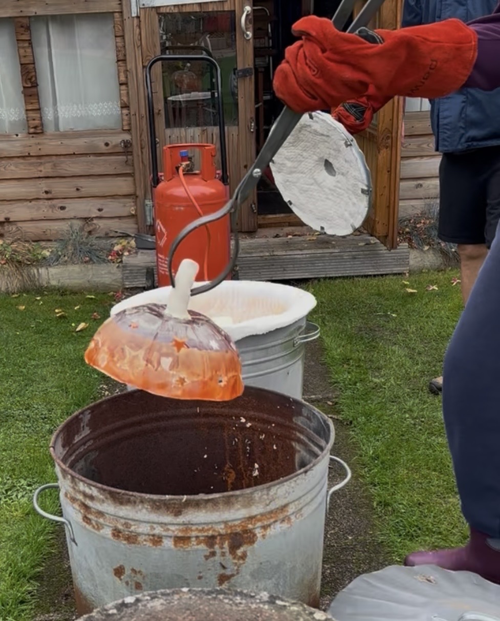 A glowing ceramic piece being lifted from the Raku kiln with tongs